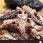 One smoked pork butt pulled apart beside the remaining whole half on a wooden cutting board.