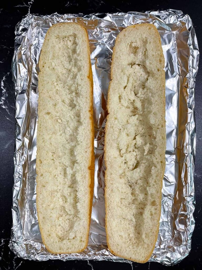Two halves of French bread scooped out on an aluminum foil lined pan.