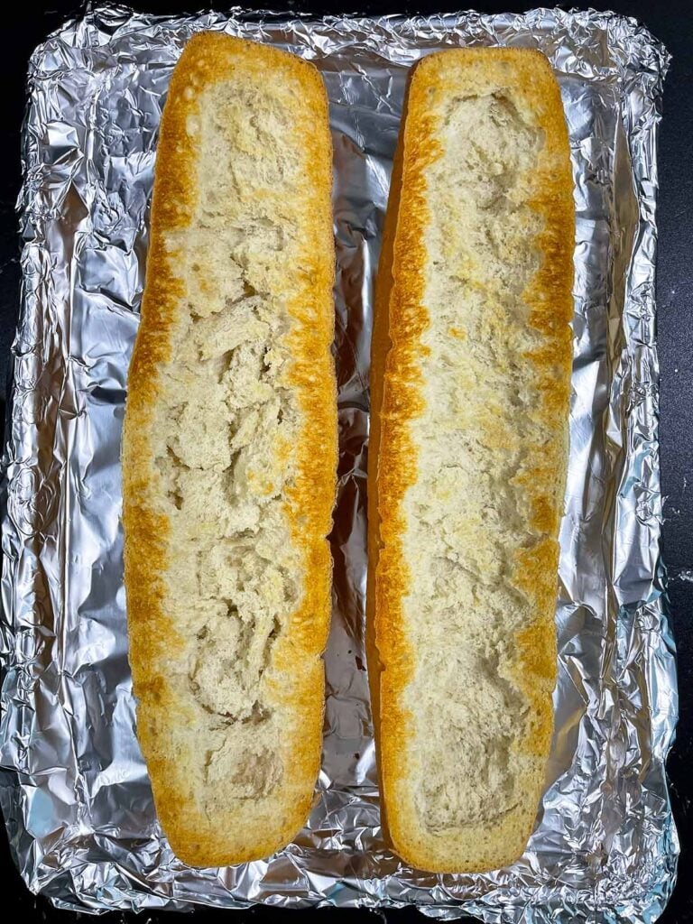 Two halves of French bread toasted on a lined pan.