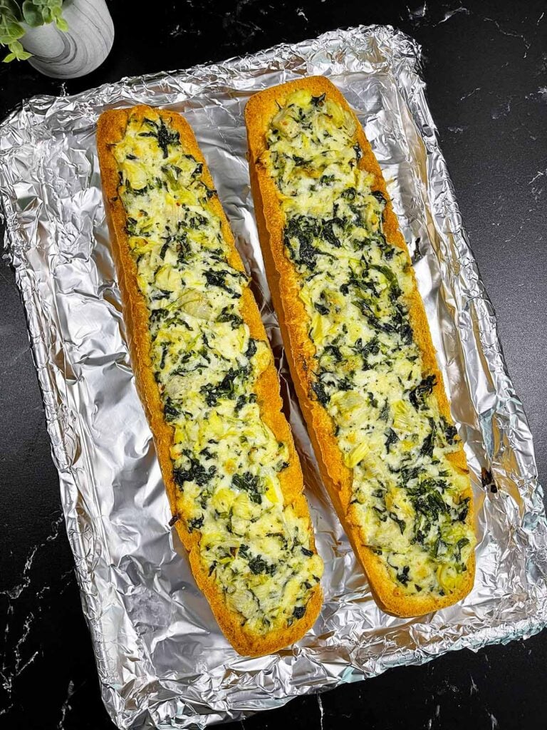 Baked spinach artichoke French bread pizza on a lined baking sheet.