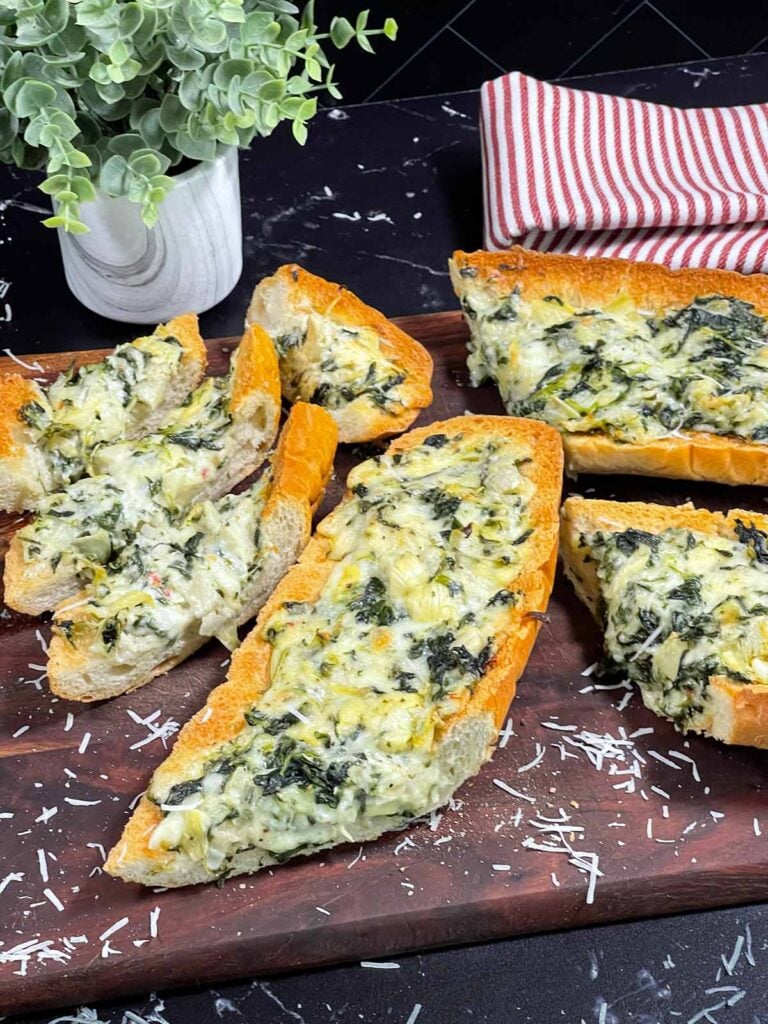 Spinach artichoke French bread pizza sliced on a wooden board.