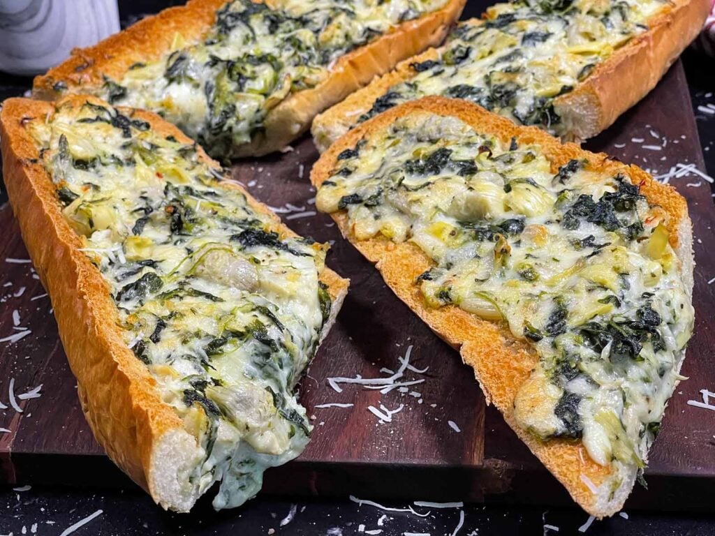 Spinach artichoke French bread pizza sliced on a wooden board.