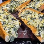 Spinach artichoke French bread pizza sliced on a wooden board.