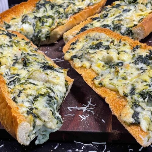 Spinach artichoke French bread pizza sliced on a wooden board.