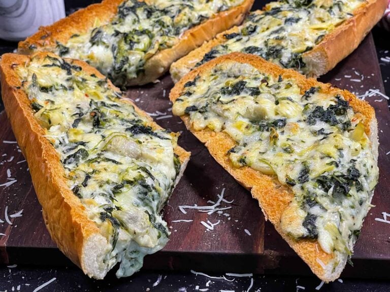 Spinach artichoke French bread pizza sliced on a wooden board.