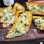 Spinach artichoke French bread pizza sliced on a wooden board.