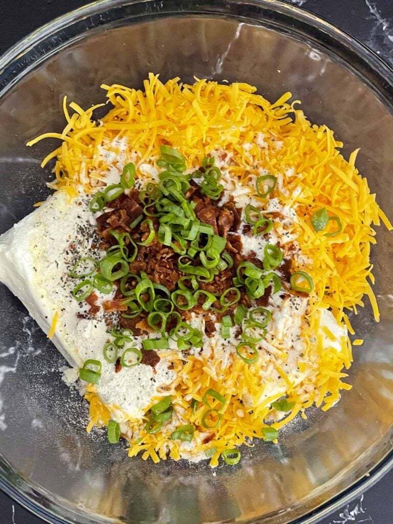 Softened cream cheese, finely shredded sharp cheddar cheese, seasonings, diced bacon, and green onions in a mixing bowl ready to make a Bacon Cheddar Ranch Cheese Ball.