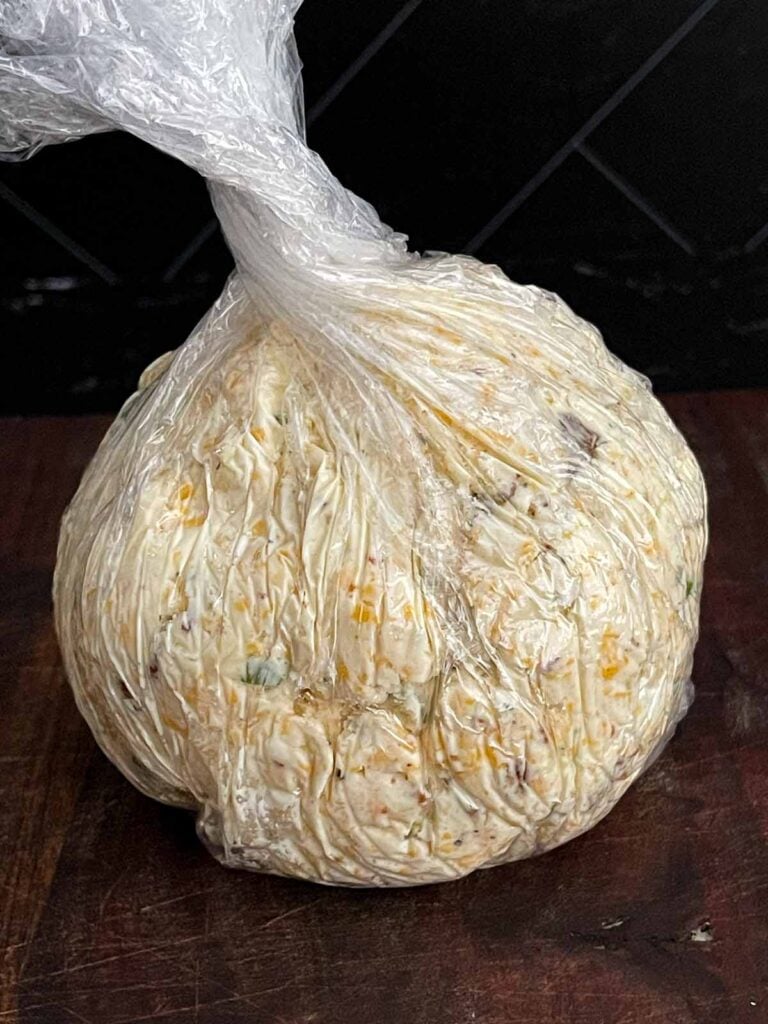 Cheese ball mixture wrapped in plastic wrap and shaped into a ball before chilling.