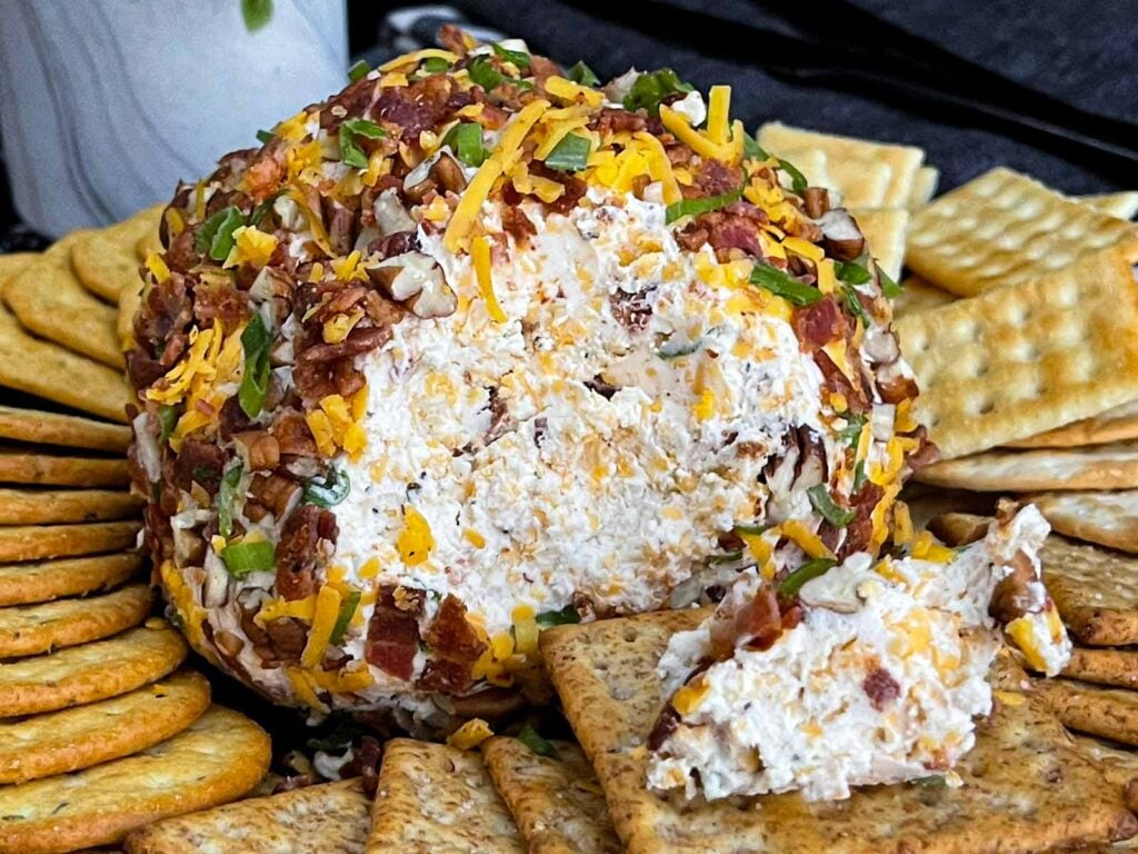 Close-up of a Bacon Cheddar Ranch Cheese Ball with a creamy cheddar center surrounded by crispy bacon and pecans.
