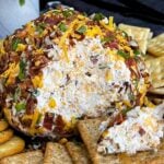 Close-up of a Bacon Cheddar Ranch Cheese Ball with a creamy cheddar center surrounded by crispy bacon and pecans.