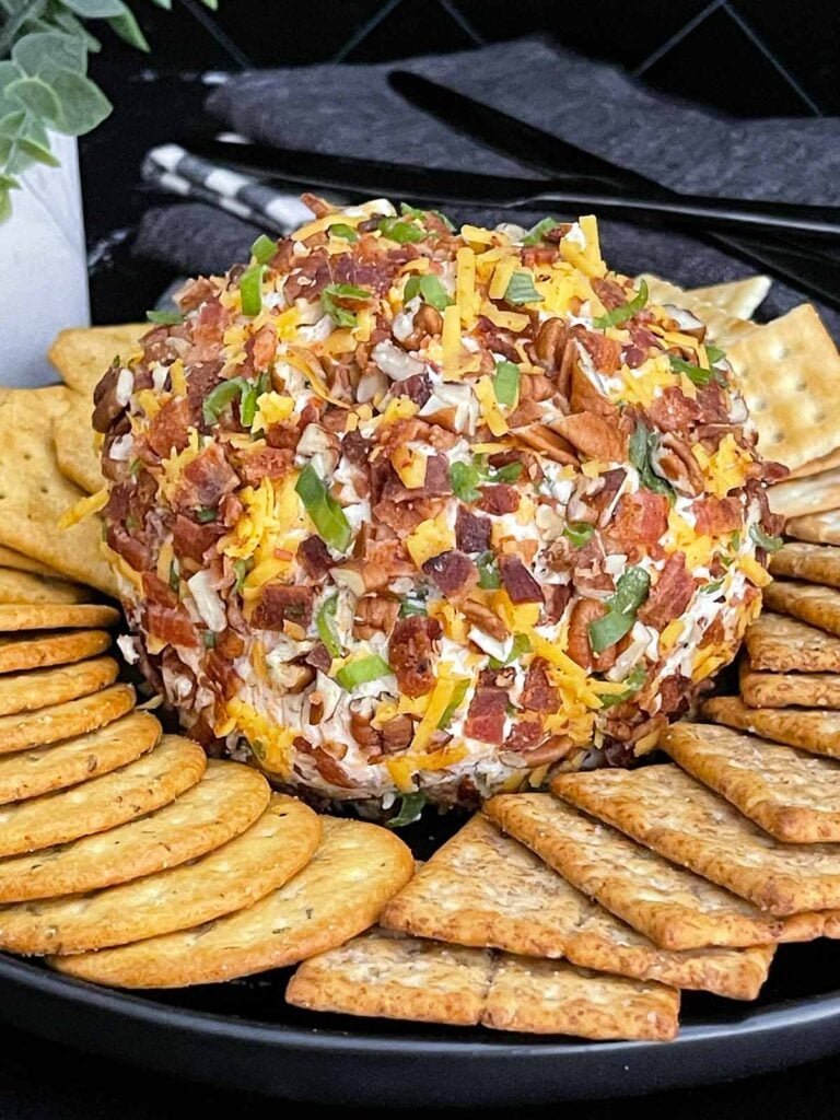 Bacon Cheddar Ranch Cheese Ball coated with bacon, pecans, cheddar cheese, and green onions served with crackers.