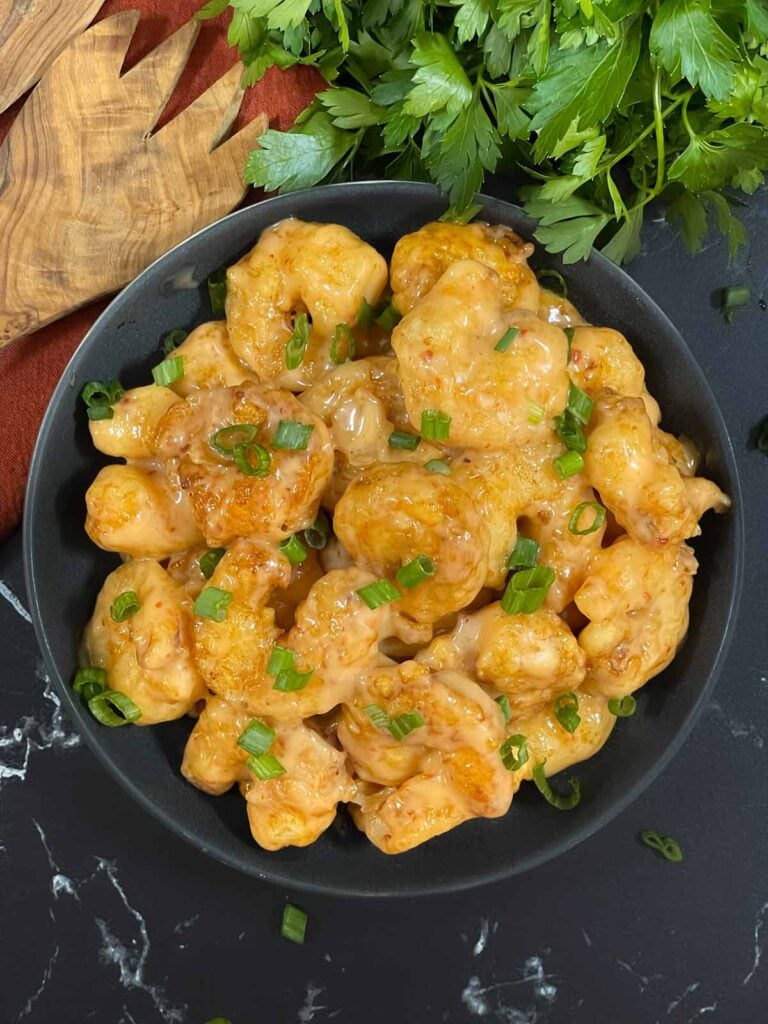 Homemade Bang Bang Shrimp served in a gray bowl and garnished with sliced green onions.