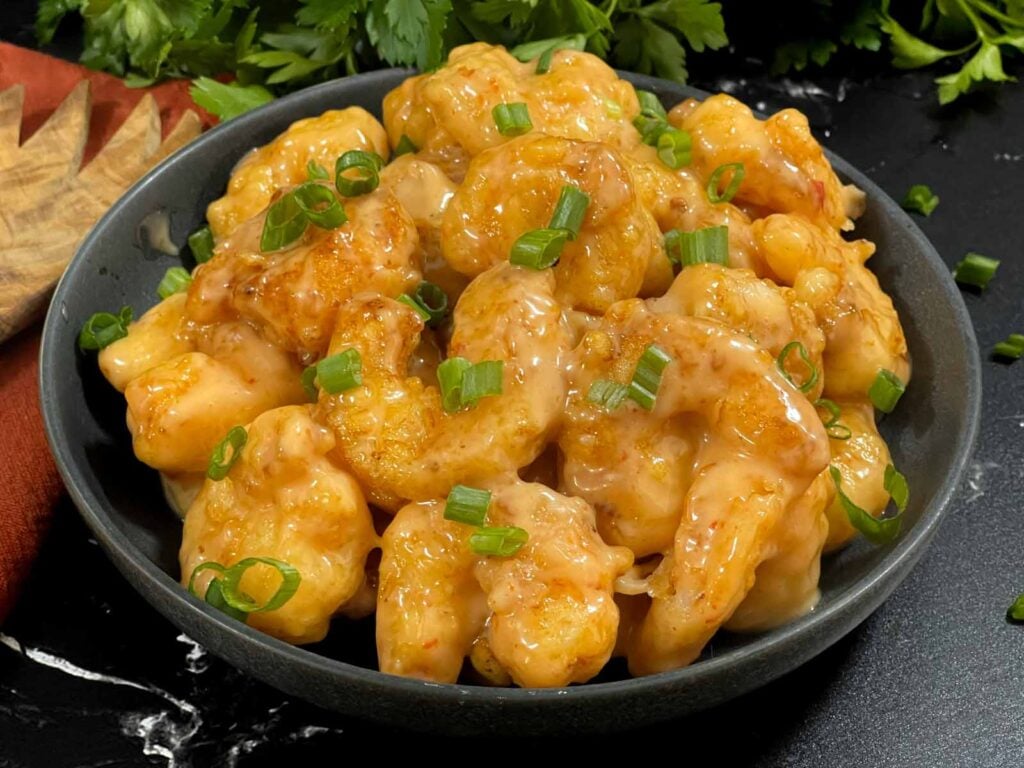 Homemade Bang Bang Shrimp served in a gray bowl and garnished with sliced green onions.