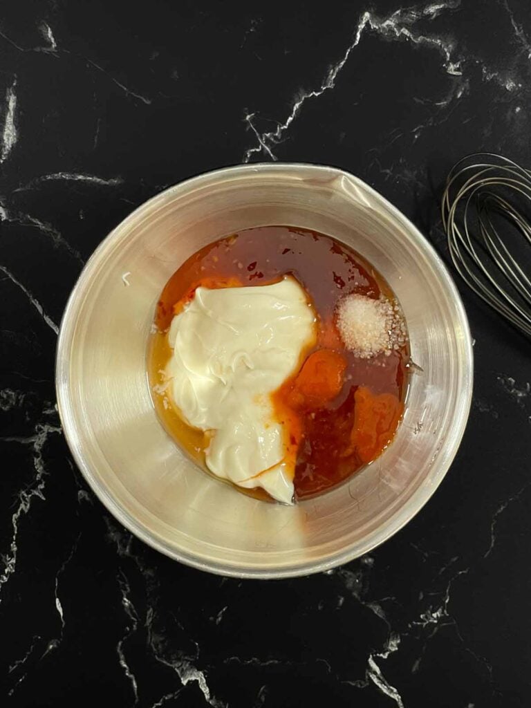 Miracle Whip, sweet chili sauce, sriracha, rice wine vinegar, and salt measured in a bowl before mixing.