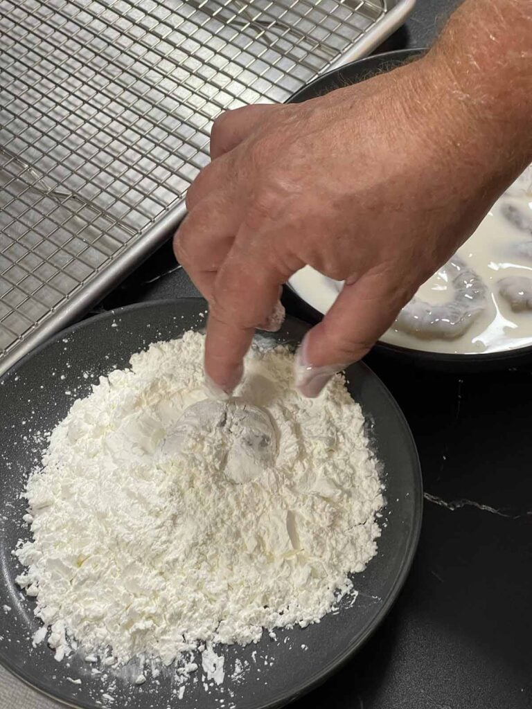 Shrimp being coated in cornstarch for a light, crispy coating before frying.