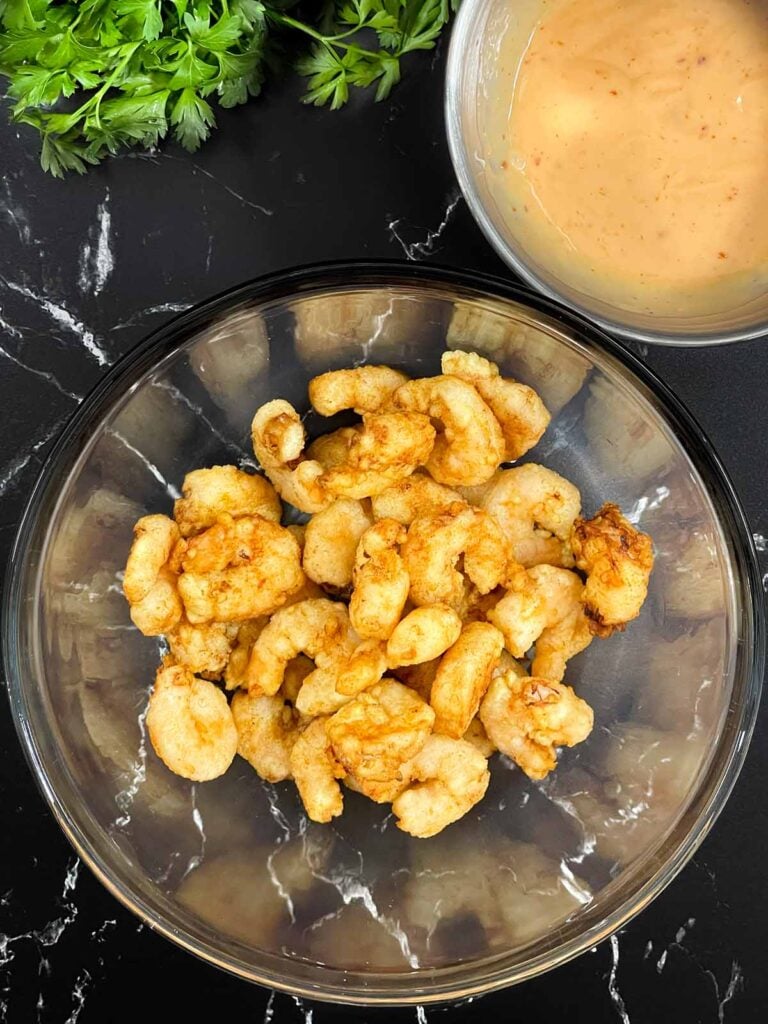 Freshly fried shrimp in a glass bowl with homemade Bang Bang sauce ready for tossing.