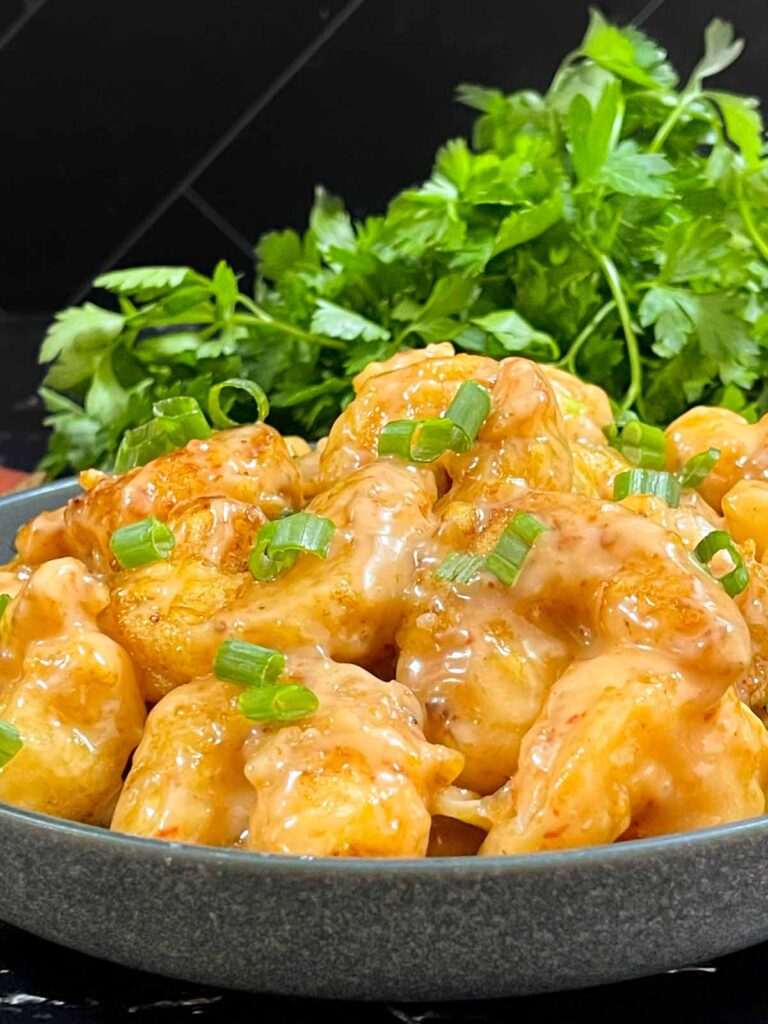 Homemade Bang Bang Shrimp served in a gray bowl and garnished with sliced green onions.