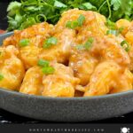 Homemade Bang Bang Shrimp served in a gray bowl and garnished with sliced green onions.