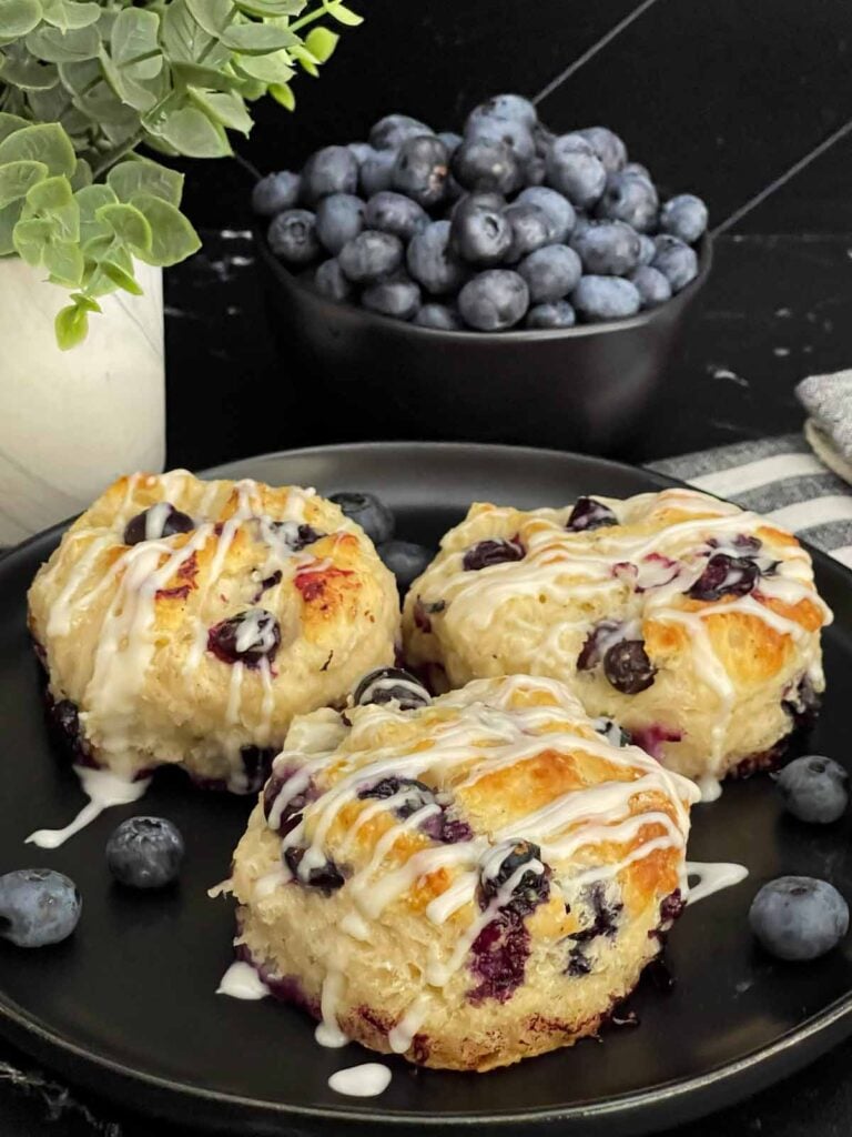 Blueberry biscuits served on a plate with fresh blueberries alongside.