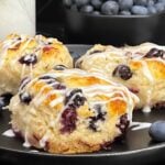 Blueberry biscuits served on a plate with fresh blueberries alongside.