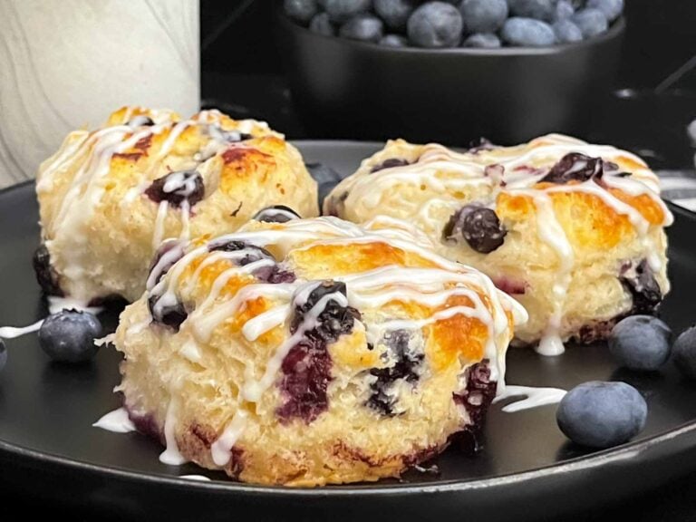 Blueberry biscuits served on a plate with fresh blueberries alongside.