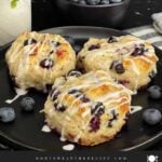 Close-up of a flaky blueberry biscuit with vanilla glaze and fresh blueberries inside.