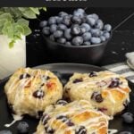 Close-up of a flaky blueberry biscuit with vanilla glaze and fresh blueberries inside.