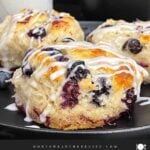 Close-up of a flaky blueberry biscuit with vanilla glaze and fresh blueberries inside.