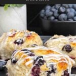 Close-up of a flaky blueberry biscuit with vanilla glaze and fresh blueberries inside.