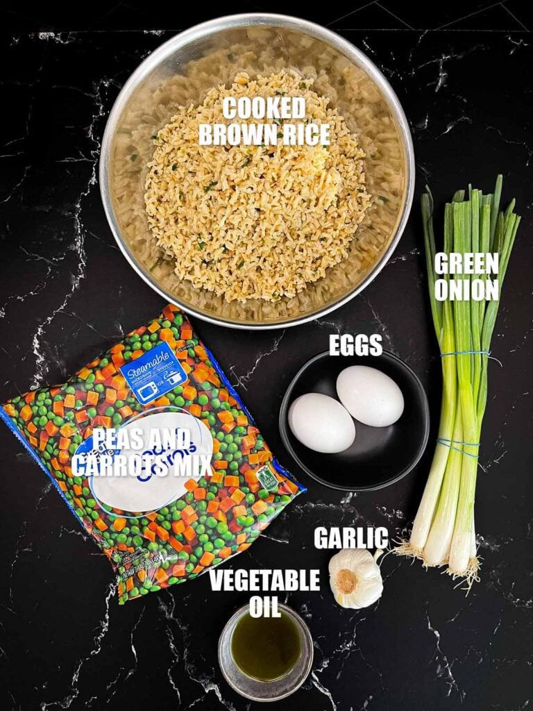Ingredients for brown fried rice including cooked brown rice, peas and carrots, eggs, green onions, garlic, and vegetable oil.