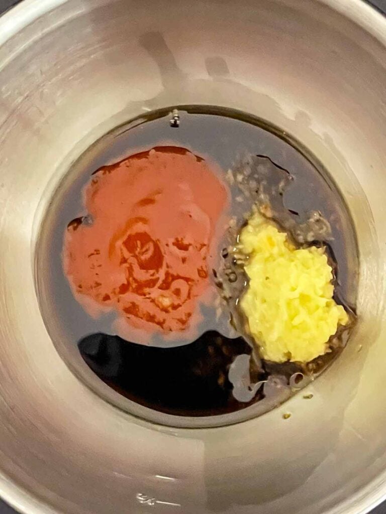 Soy sauces, Sriracha, sesame oil, and grated ginger combined in a stainless steel bowl before mixing for brown fried rice.