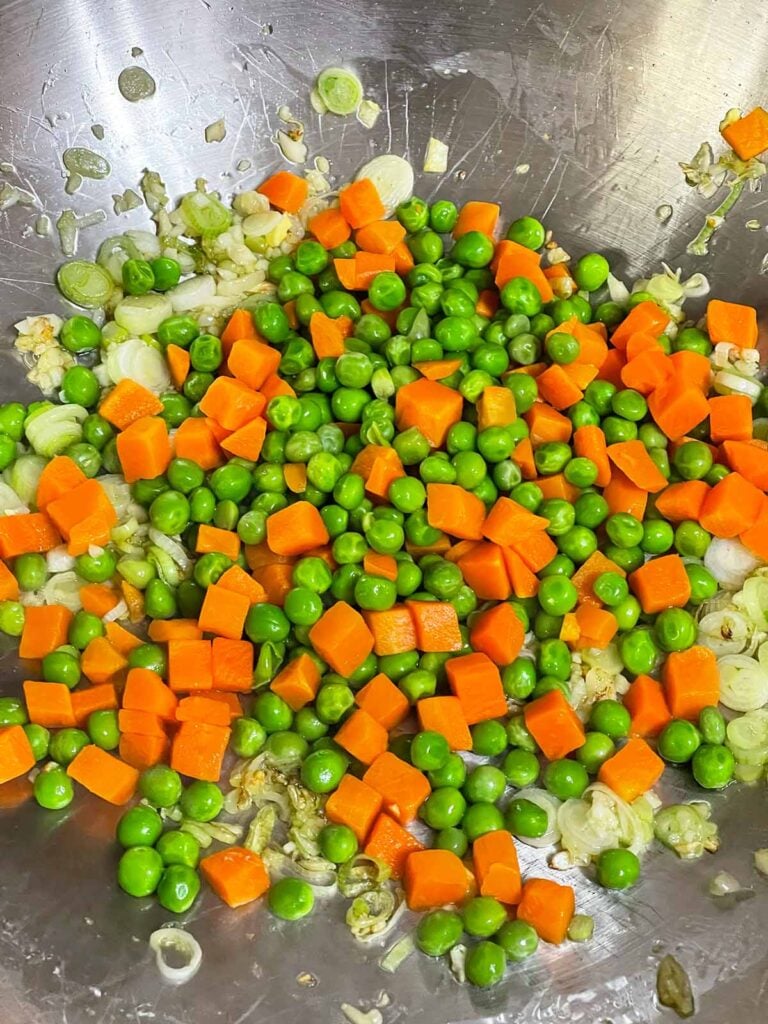 Frozen peas and carrots cooking with garlic and green onions in a wok.