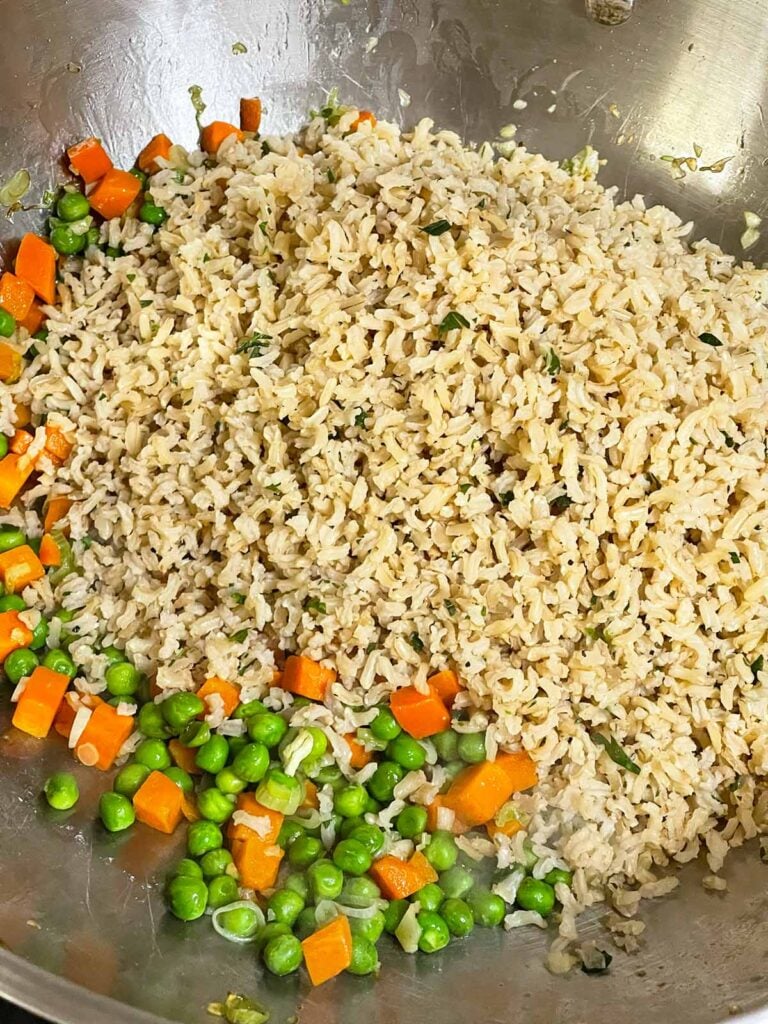 Cold cooked brown rice added to the wok with peas and carrots.