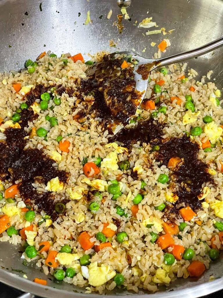 Homemade fried rice sauce poured over brown rice in a hot wok.