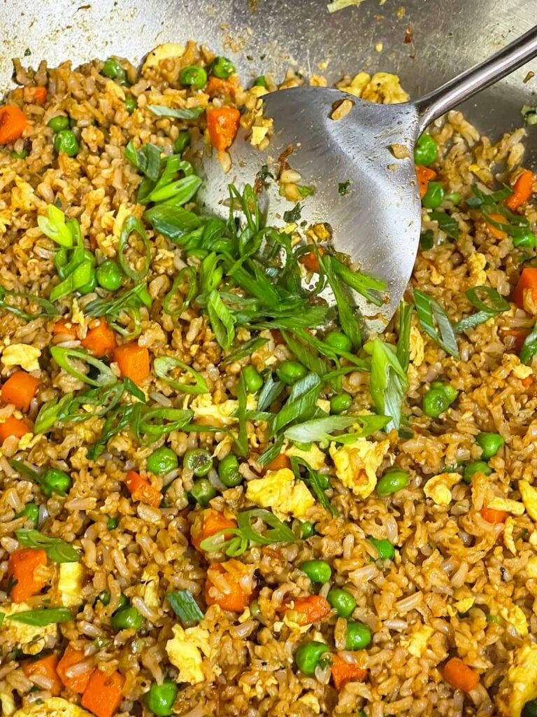Sliced green onions sprinkled over homemade brown fried rice before the final toss.