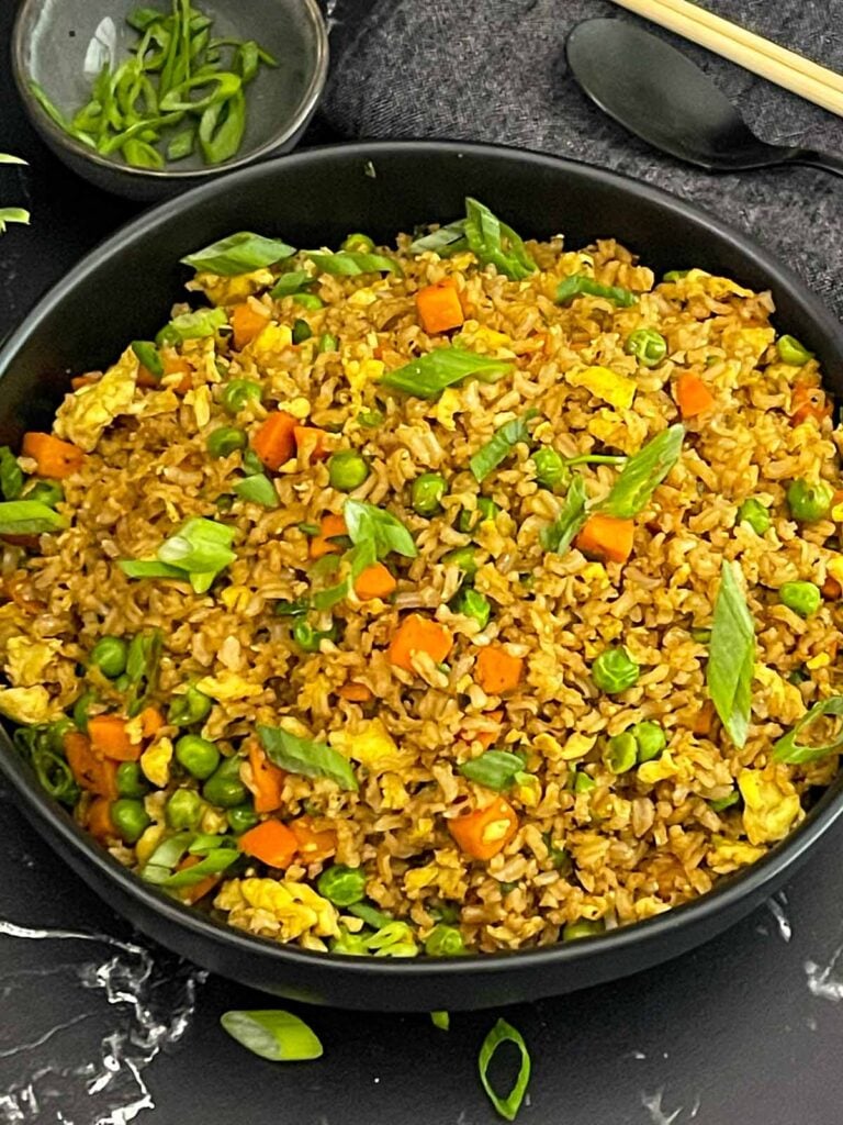 Brown fried rice served in a bowl with eggs, peas, carrots, and green onions.