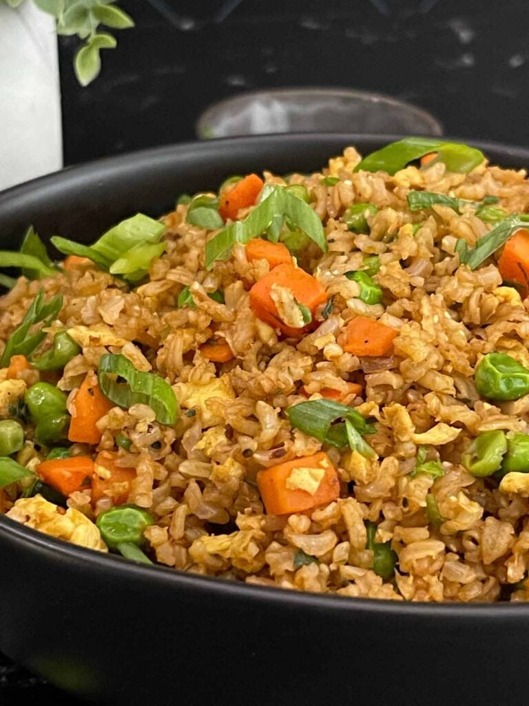 Brown fried rice served in a bowl with eggs, peas, carrots, and green onions.