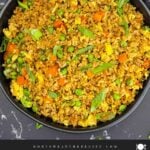 Brown fried rice served in a bowl with eggs, peas, carrots, and green onions.