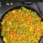 Brown fried rice served in a bowl with eggs, peas, carrots, and green onions.