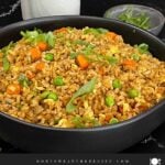Brown fried rice served in a bowl with eggs, peas, carrots, and green onions.