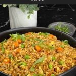 Brown fried rice served in a bowl with eggs, peas, carrots, and green onions.