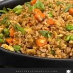 Brown fried rice served in a bowl with eggs, peas, carrots, and green onions.