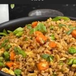 Brown fried rice served in a bowl with eggs, peas, carrots, and green onions.