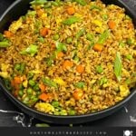 Brown fried rice served in a bowl with eggs, peas, carrots, and green onions.