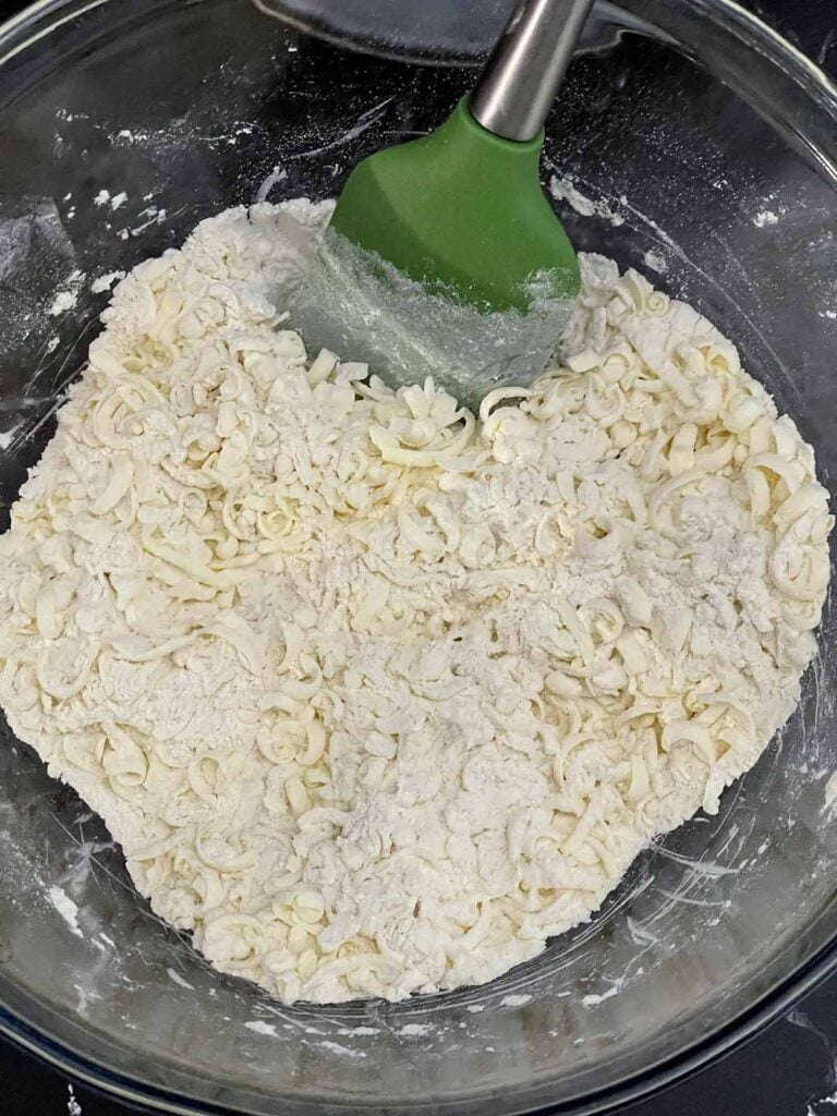 Dry ingredients and frozen shredded butter mixed together in a large bowl for cheddar dill biscuits.