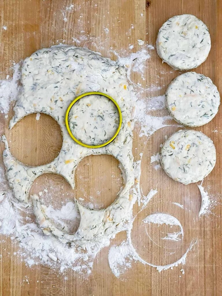 Cheddar dill biscuit dough patted into a rectangle and cut with a round biscuit cutter.