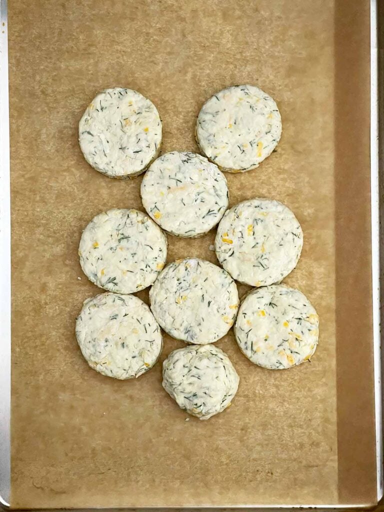 Unbaked cheddar dill biscuits placed touching on a parchment paper lined baking sheet.
