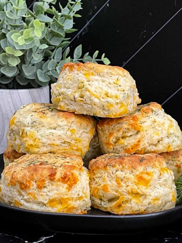 Freshly baked cheddar dill biscuits brushed with garlic dill butter stacked on a black plate.