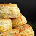Freshly baked cheddar dill biscuits brushed with garlic dill butter stacked on a black plate.