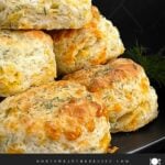 Freshly baked cheddar dill biscuits brushed with garlic dill butter stacked on a black plate.